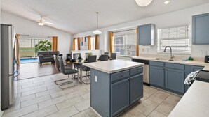 A modern kitchen with blue cabinets, a central island, and a dining area with a pool view. - Great Community, Amazing Private Pool, Near Disney! (Davenport)