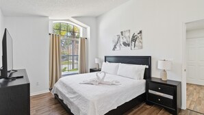 A modern bedroom with a large bed, a TV on a stand, and a window with curtains. - Great Community, Amazing Private Pool, Near Disney! (Davenport)