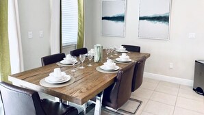 A dining area with a wooden table set for four, surrounded by chairs, with two framed artworks on the wall. - Amazing 4/3 Home at Reunion!! With Private Pool, Near Disney and Universal!! (Kissimmee)