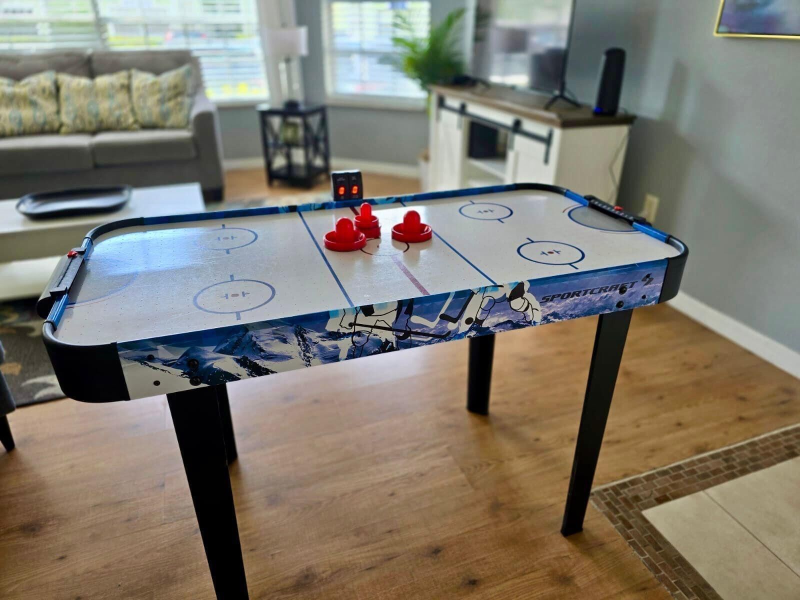 Um jogo de hóquei de mesa em uma sala de estar, com um sofá e uma televisão ao fundo.