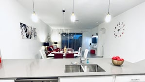 Een moderne keuken met een roestvrijstalen spoelbak, witte kasten en een eethoek met een rode tafel en stoelen.
