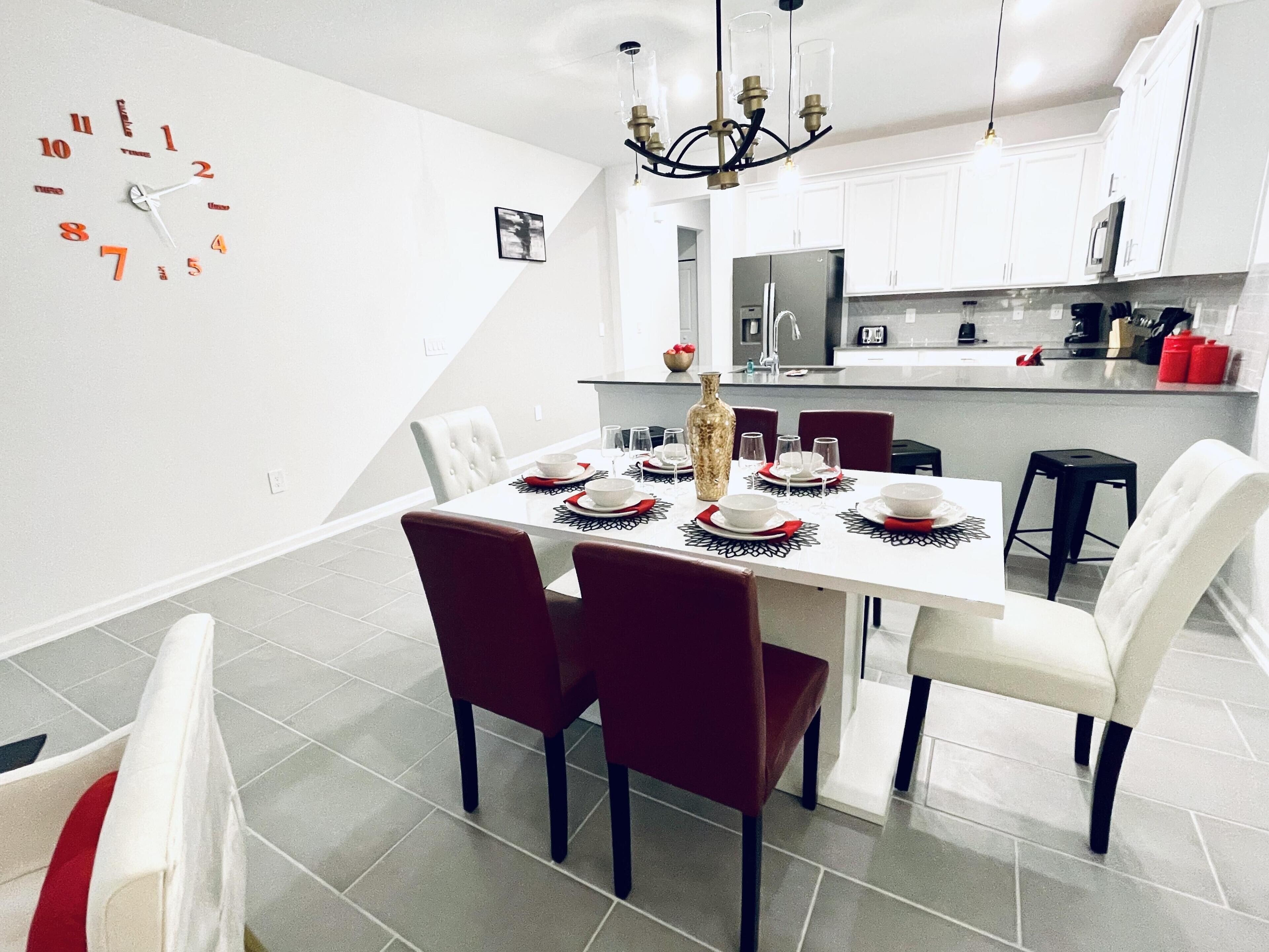A modern kitchen with white cabinets, a stainless steel refrigerator, and a dining area with a white table set for four.