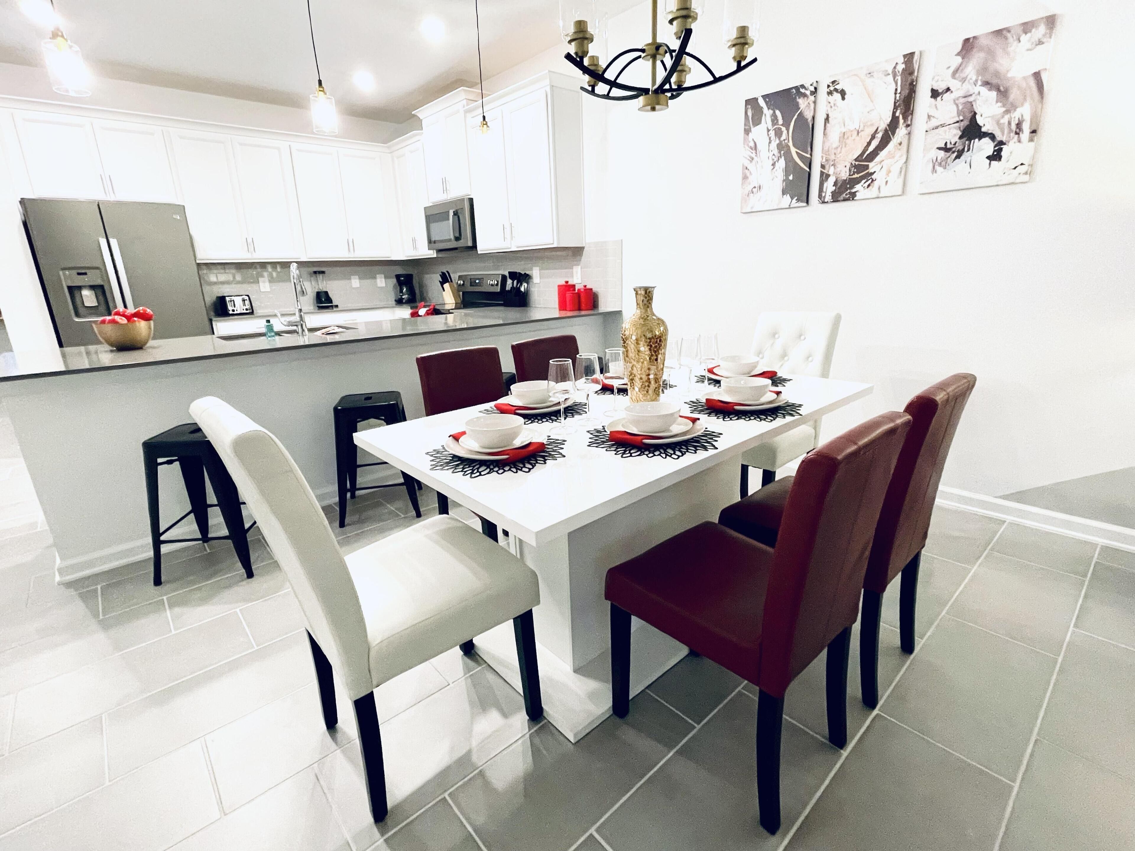 A modern kitchen with white cabinets, a dining table set with red and white plates, and a large vase.