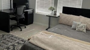 Une chambre à coucher avec un lit, un bureau et deux fenêtres équipées de stores.