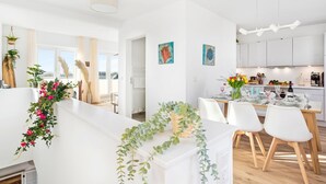 Una cocina moderna con armarios blancos, un comedor con mesa y sillas blancas, y una sala de estar con sofá blanco y una planta.