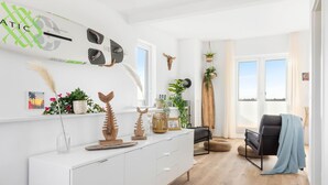 Una sala de estar moderna con un sofá blanco, un sillón negro y una mesa de centro de madera. Hay elementos decorativos como un cráneo de vaca y un esqueleto de pez en la pared.
