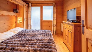 A wooden cabin room with a bed, a television, and a window with curtains.
