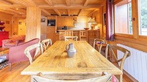 A wooden dining table with chairs, a kitchen area with cabinets, a red cabinet, and a window with curtains.