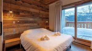 A wooden-paneled room with a bed, bench, and large window with a view of a snowy landscape.