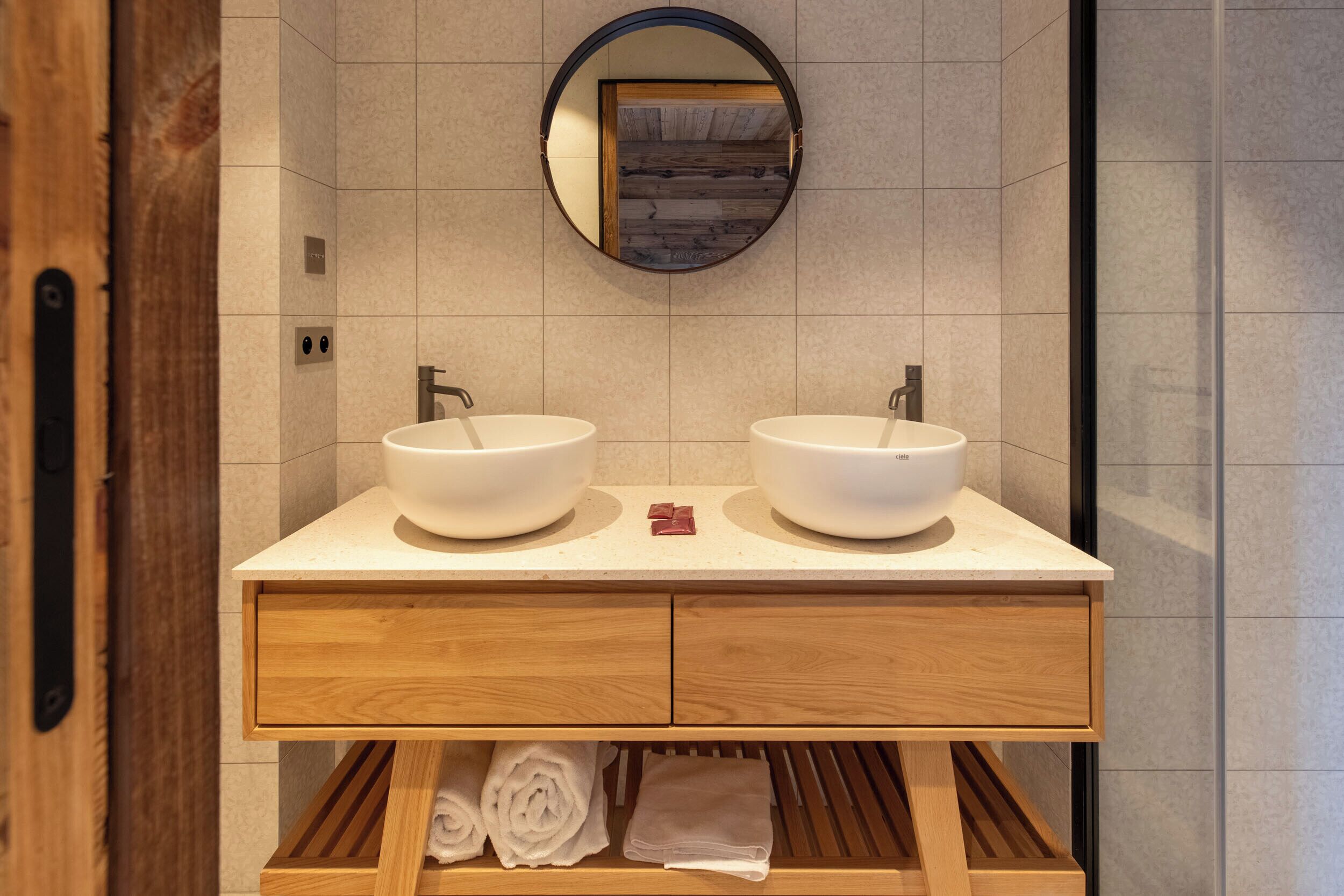A bathroom with two sinks, a wooden vanity, a mirror, and a towel rack.