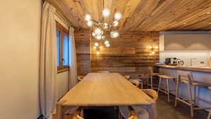 A wooden interior with a dining table and chairs, a kitchen area with cabinets, and a ceiling light fixture.