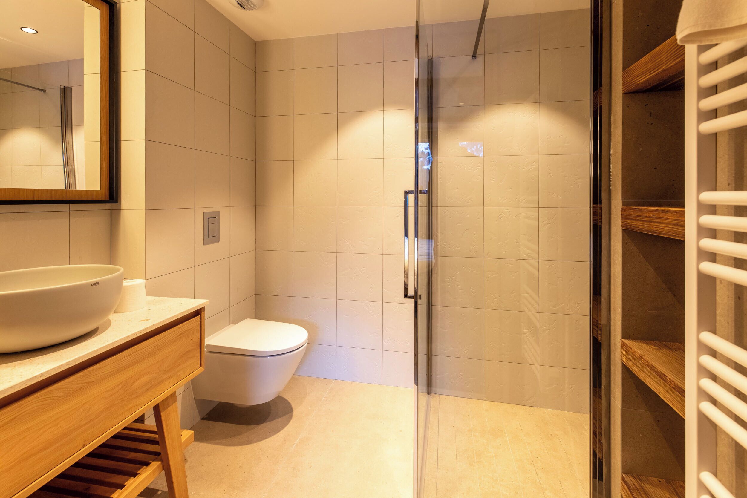 Une salle de bain moderne avec une douche à parois de verre, un meuble-lavabo en bois et des toilettes blanches.