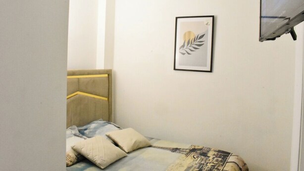 Un dormitorio con cama, cabecera, una obra de arte enmarcada en la pared y una ventana con persiana.