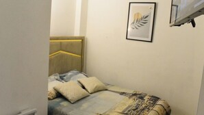 Un dormitorio pequeño con cama, almohadas, un cuadro enmarcado en la pared y un televisor montado.