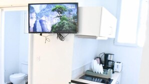 Cocina compacta con un televisor sobre la encimera, un pequeño comedor con una mesa preparada para dos personas y un lavamanos a la vista.