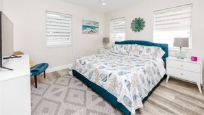 A bedroom with a bed, a desk, a chair, a ceiling fan, and a window with blinds.
