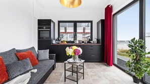 A modern living room with a sofa, a coffee table with flowers, a kitchen area with cabinets and a window, and a view of the outdoors. - Pet friendly apartment in Olpenitz (Olpenitz)