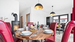 A modern dining room with a round wooden table set for four, red leather chairs, a black and gold pendant light, and a wood-burning stove. - Pet friendly apartment in Olpenitz (Olpenitz)