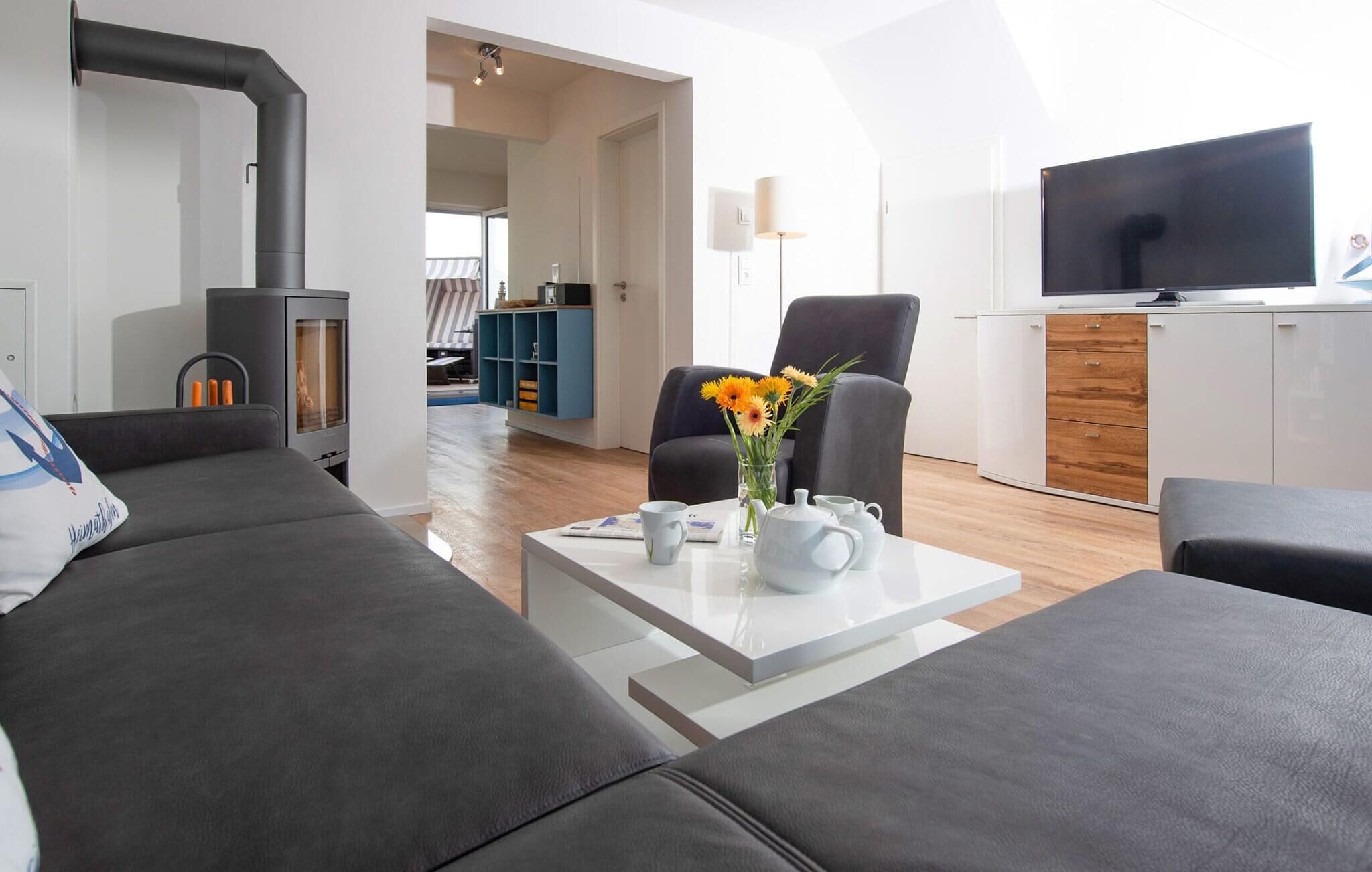 A modern living room with a sofa, a coffee table with a vase of flowers, a TV, and a fireplace.