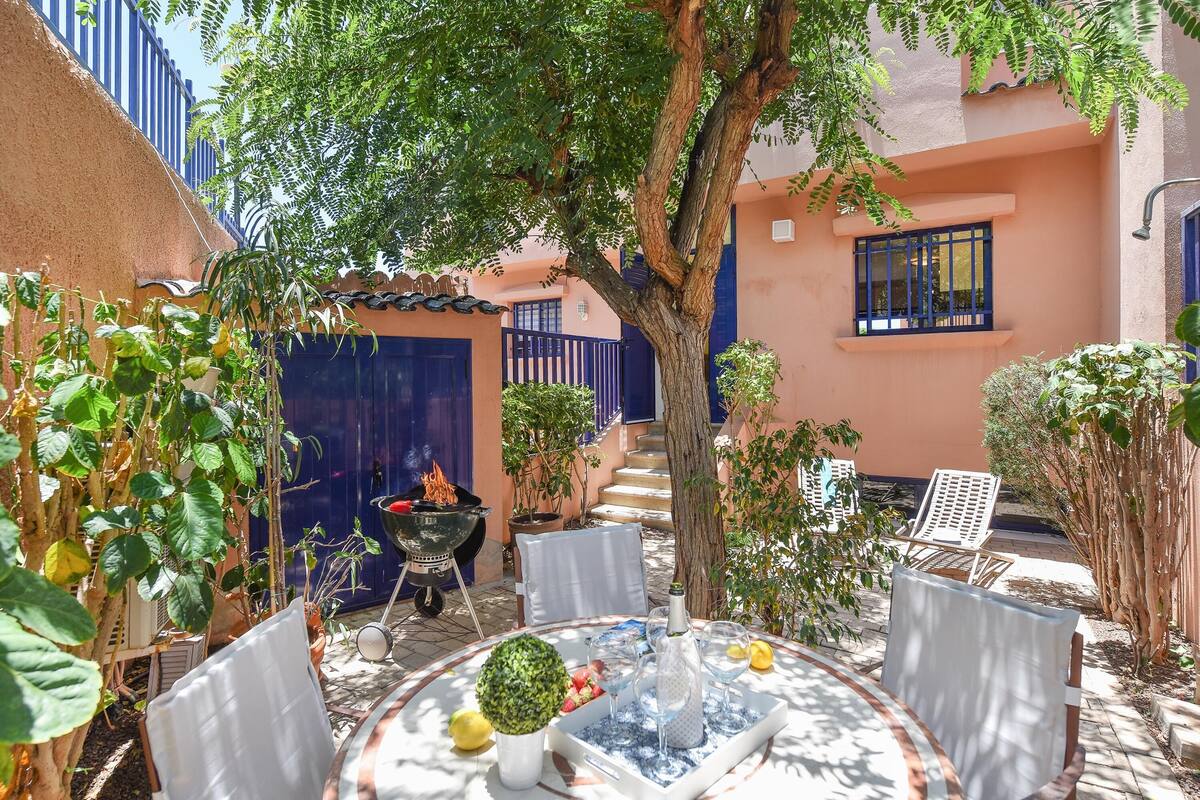 A patio with a round table, chairs, a grill, and potted plants.