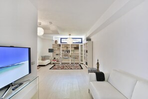 A modern living room with a flat-screen TV, white sofas, a glass coffee table, and a bookshelf. - Meloneras Duplex (San Bartolomé de Tirajana)