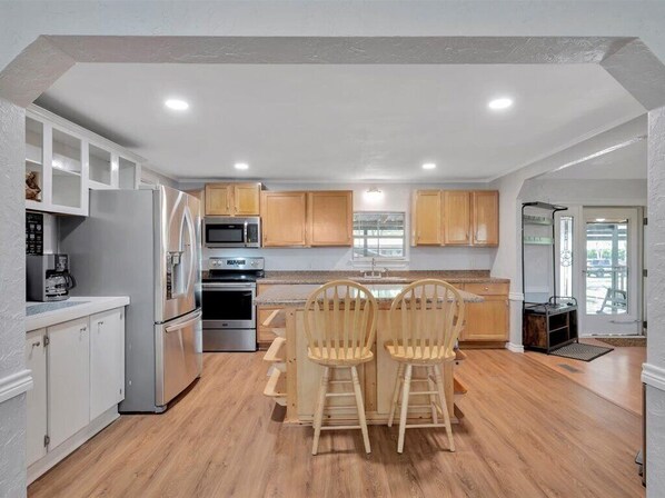 A modern kitchen with white cabinets, stainless steel appliances, and a wooden dining area. - Lake Sam Rayburn Access! (Zavalla)