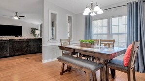 Un coin repas avec une table en bois, des bancs et des chaises. Un lustre est suspendu au-dessus de la table.