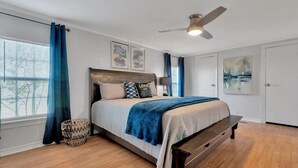 Une chambre à coucher avec un lit, un ventilateur de plafond, une fenêtre avec des rideaux et une porte.