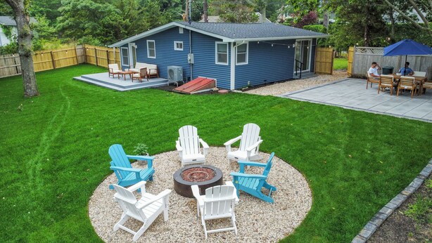 Un giardino sul retro con una casa blu, un braciere e un'area salotto all'aperto.
