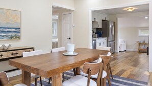 Un'area pranzo con un tavolo e sedie in legno, una cucina sullo sfondo e un quadro appeso al muro.