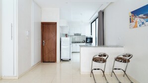 A modern kitchen with white cabinets, a wooden door, and a small island with two bar stools. - Apartment Near the Beach (Bouznika)