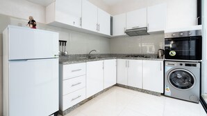 A modern kitchen with white cabinets, a granite countertop, a built-in oven, and a washing machine. - Apartment Near the Beach (Bouznika)