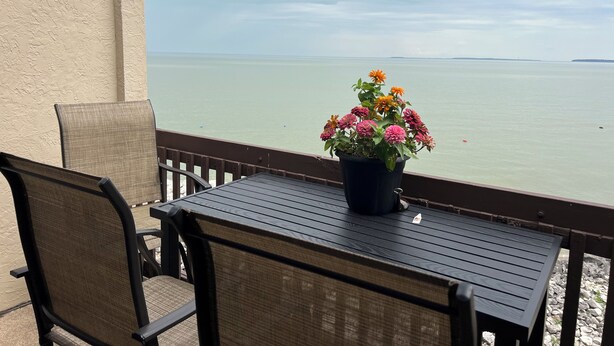 Un balcón con una mesa y sillas, con vista a una masa de agua tranquila.