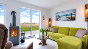 A modern living room with a green sofa, a glass coffee table, a fireplace, and a large window with a view of the outdoors. - Gorgeous home in Olpenitz with sauna (Olpenitz)