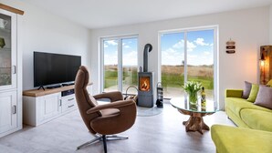 A modern living room with a flat-screen TV, a comfortable brown chair, a glass coffee table, a green sofa, and a wood-burning stove. - Gorgeous home in Olpenitz with sauna (Olpenitz)