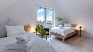 A modern bedroom with two beds, a view of the city, and a green chair. - Gorgeous home in Olpenitz with sauna (Olpenitz)