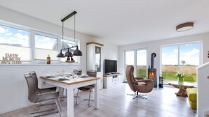 A modern living room with a dining area, a fireplace, and large windows offering a view of the outdoors. - Gorgeous home in Olpenitz with sauna (Olpenitz)