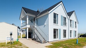 Ein zweistöckiges Haus mit überdachter Veranda und einer Treppe, die zum Obergeschoss führt.