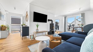 Ein modernes Wohnzimmer mit Flachbildfernseher, einer großen Couch, einem Holztisch und einem Essbereich mit Tisch und Stühlen.