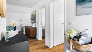 Ein modernes Wohnzimmer mit Holzboden, einer schwarzen Couch, einer weißen Vase mit Blumen und einem Bild an der Wand.