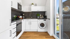 Eine moderne Küche mit weißen Schränken, einem Einbauofen, einer Waschmaschine und einer Kaffeemaschine.