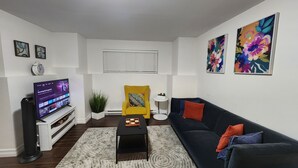 A living room with a TV, a yellow armchair, a black sofa, and two floral paintings on the wall. - Private apartment in Moncton (Moncton)