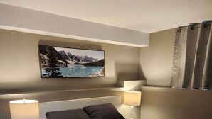 A bedroom with a bed, two bedside tables, a nightstand, a lamp, a picture on the wall, and a window with curtains. - Private apartment in Moncton (Moncton)