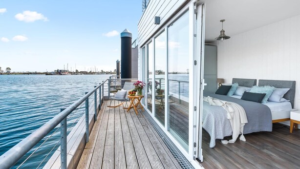 A modern room with a large window, a bed with grey bedding, and a view of the water. - Stunning ship in Olpenitz with sauna (Olpenitz)