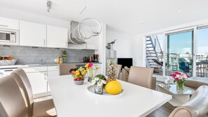 A modern kitchen with white cabinets, a microwave, and a dining area with a white table and chairs. There are flowers on the table and a view of a cityscape through large windows. - Stunning ship in Olpenitz with sauna (Olpenitz)