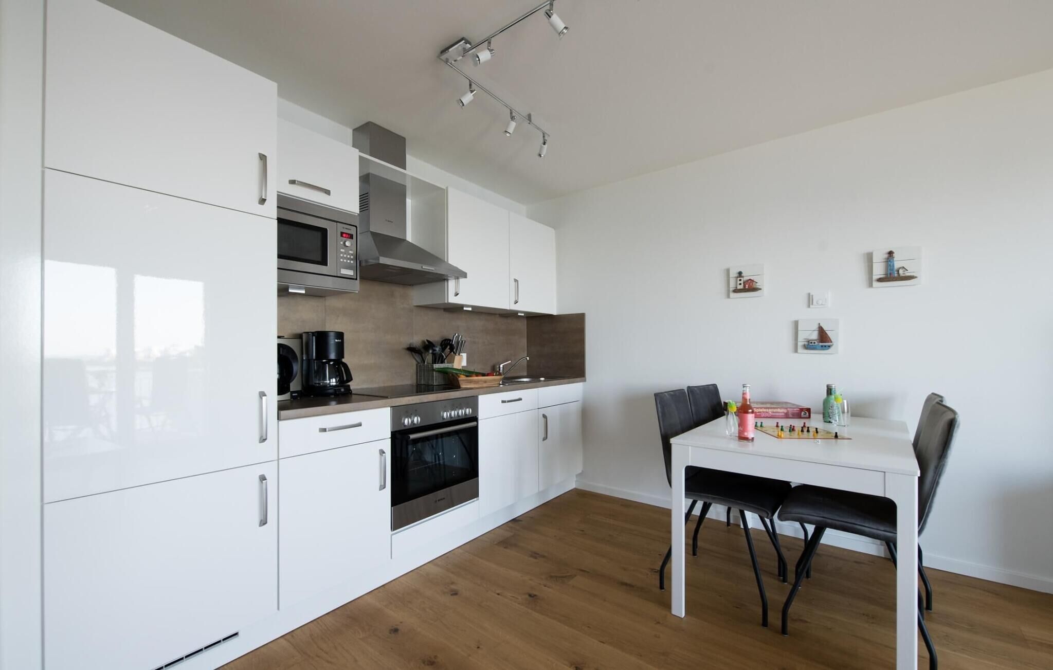 A modern kitchen with white cabinets, stainless steel appliances, and a wooden floor. There is a dining table with chairs and a chessboard on the table.