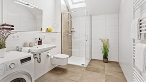 Un baño moderno con lavadora incorporada, ducha con cerramiento de vidrio y tragaluz.