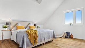 Un dormitorio con cama, mesitas de noche, una ventana y una planta en maceta.