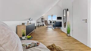 Un dormitorio estilo loft moderno con techo inclinado, un ventanal grande, un sofá, un escritorio y un comedor.