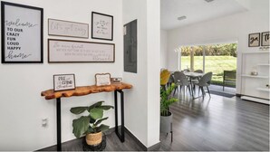 Un interior moderno con comedor, una pared decorada con citas motivacionales y una consola de madera con una planta.